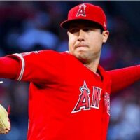 A baseball player wearing a red jersey and cap with an "A" logo is pitching. His arm is extended mid-throw, and he holds a baseball in his hand. The background is blurred, focusing on the pitcher, creating a compelling image for Overdose Awareness Day to highlight the importance of addressing opiate use. CA Norml
