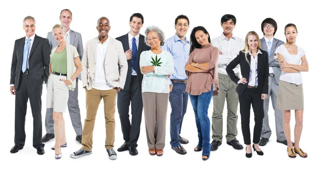 A diverse group of 12 adults stand in a row, facing the camera. They are dressed in a variety of outfits ranging from casual to business attire. One woman is holding a cannabis leaf symbol on her shirt, representing Cal NORML's 2019 accomplishments. The background is plain white. CA Norml