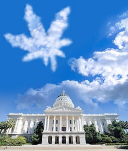 A grand, white, neoclassical government building stands under a clear blue sky with some clouds. Unusually, a large cloud shaped like a cannabis leaf floats prominently in the sky above the California Legislature. Trees and greenery surround the building. CA Norml