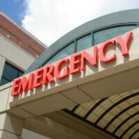 Entrance to an emergency room at a hospital, marked by a prominent red "EMERGENCY" sign above a covered walkway, set against a backdrop of a light-colored building and partly cloudy sky. This California facility is equipped to handle various situations, including RAP-C incidents and cannabis overdoses. CA Norml