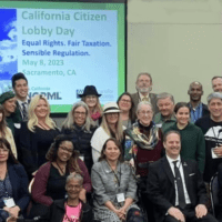 A large, diverse group of people is posing for a group photo in front of a screen displaying "Citizen Lobby Day in Sacramento 5/8/2023." The slide mentions "Equal Rights, Fair Elections, Sensible Regulation" and notes the event date as May 10, 2023, in Sacramento, CA. CA Norml
