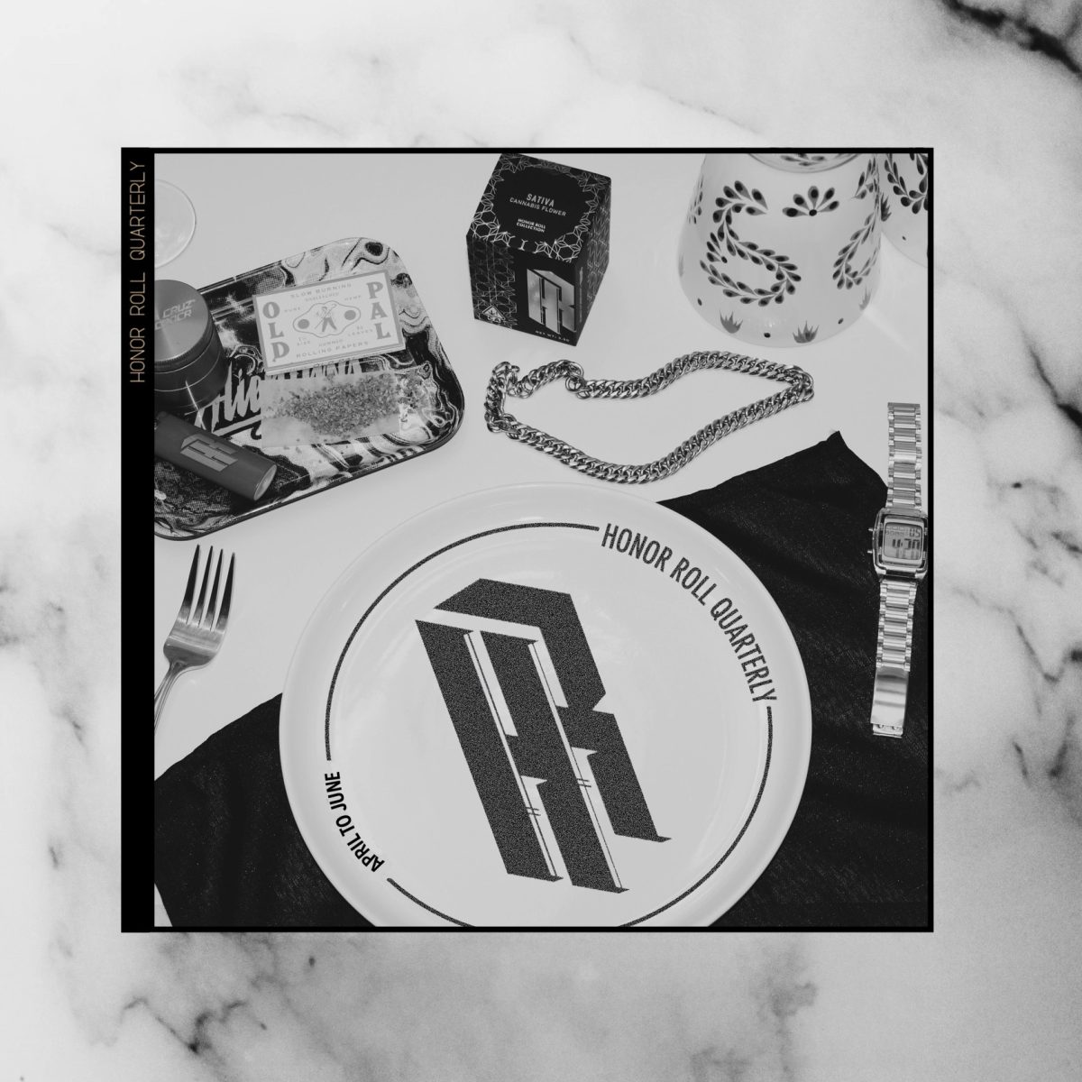 Black and white image featuring a plate with the text “Honor Roll Quarterly” and the letters "HR" stylized in the center. Surrounding items include a fork, knife, chain, watch, and a tray with various items on a marble surface. The text "Honor Roll Delivery Quarterly" borders the image. CA Norml