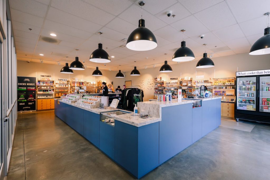 Interior view of the Embarc dispensary in Fresno, California, featuring a modern retail layout with blue counters, hanging lights, and shelves stocked with cannabis products.