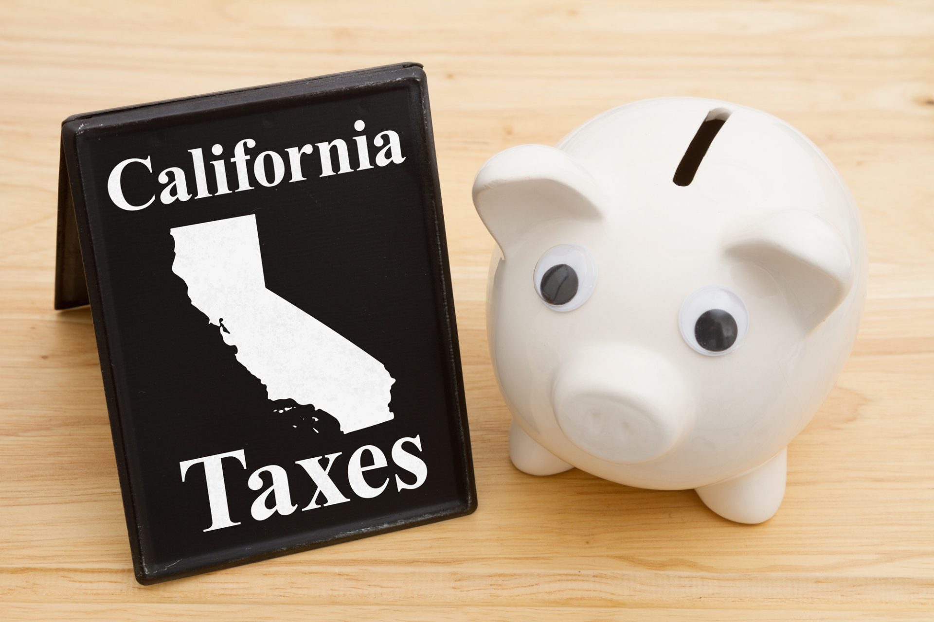 A small blackboard displaying "California Taxes" with an outline of California is on the left. On the right, a white piggy bank with googly eyes, symbolizing 280E Deductions, sits on a wooden surface. CA Norml