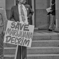 Ca NORML director Dale Gieringer standing with a sign saying "Save Marijuana Decrim" at the state capitol building, sometime in the 70s
